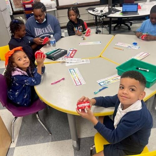 Elementary students seated around a classroom table working together with learning materials during a small group activity.
